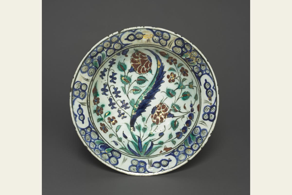 An Iznik dish with a long blue-green leaf, red flowers and a patterned rim.